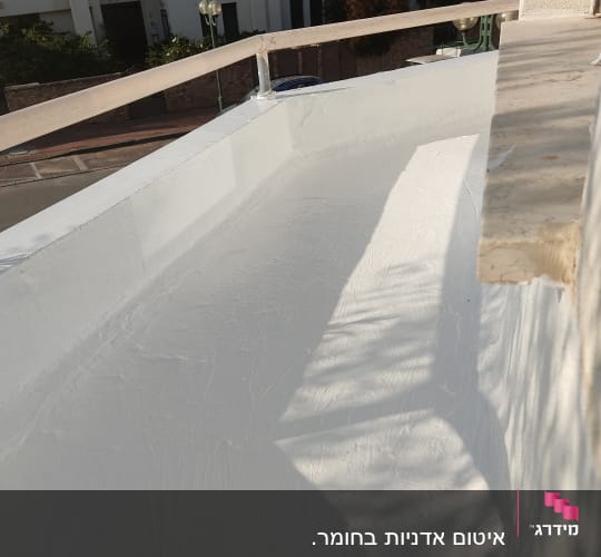 משטח אטום בלבן על גג עם מעקה מתכת